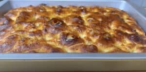 Golden brown baked focaccia bread with crispy edges in a metal baking tray.